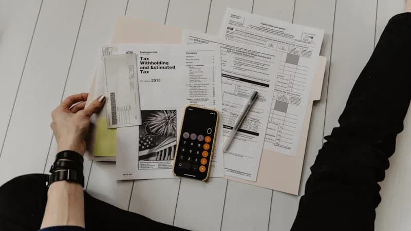 Tax documents including W-9 and W-8BEN forms for affiliate marketers with a calculator and laptop showing earnings